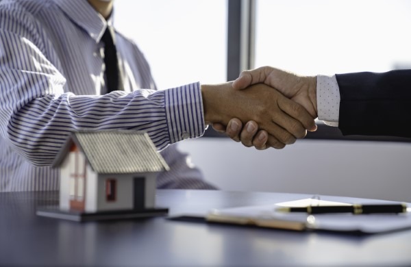 Escena de cierre de un trato en oficinas inmobiliarias, destacando la confianza y profesionalismo que ofrece Franquicias Alfa en sus servicios inmobiliarios personalizados.