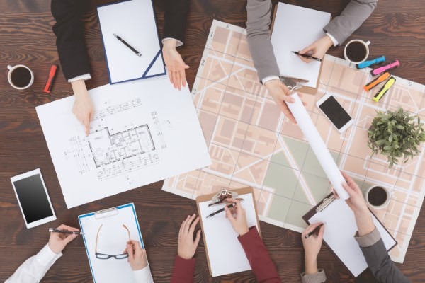 Equipo trabajando con planos en oficinas inmobiliarias, mostrando la planificación profesional que Franquicias Alfa garantiza en cada uno de sus proyectos inmobiliarios.