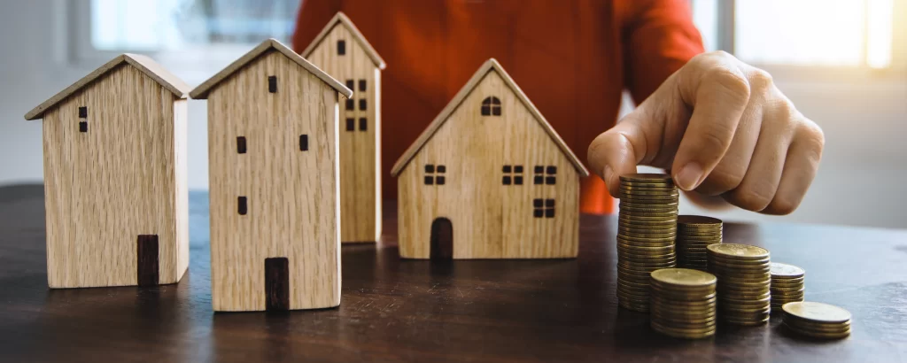 Mano apila monedas junto a casas de madera. Representa la rentabilidad y ¿Cuánto cuesta abrir una franquicia inmobiliaria en México?