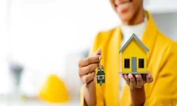 Mujer con llaves y modelo de casa para decidir Invertir en inmuebles o en una franquicia inmobiliaria: ¿Qué conviene más?