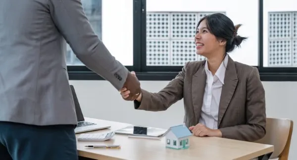 Una asesora inmobiliaria cierra un trato con un cliente en una oficina moderna, luego de explicarle claramente cómo funciona la inversión en bienes raíces.