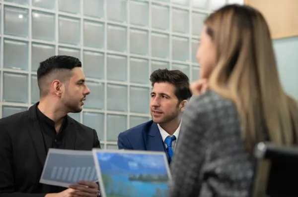 Tres profesionales del sector inmobiliario discuten estrategias en una oficina moderna. Este tipo de colaboración demuestra que es rentable ser agente inmobiliario.