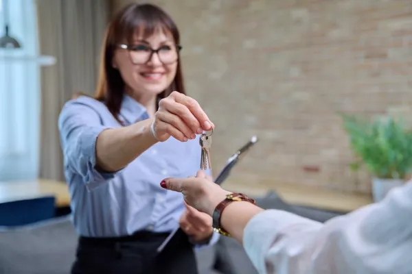 Una agente inmobiliaria sonriente entrega las llaves de una propiedad a su cliente. Este momento refleja cómo es rentable ser agente inmobiliario.