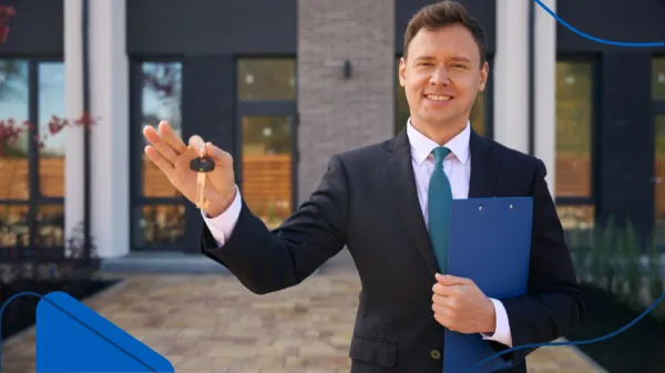 Frente a un moderno edificio, un asesor inmobiliario sonríe y muestra unas llaves, destacando uno de los momentos más gratificantes de trabajar en el sector inmobiliario.