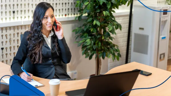 Una mujer ejecutiva trabaja desde su oficina mientras toma notas durante una llamada telefónica, en un contexto relacionado con cómo invertir en franquicias en México.