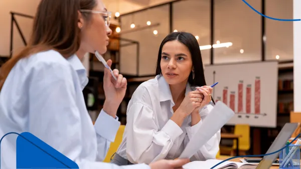 Dos mujeres conversan en una oficina mientras revisan gráficos y papeles, en una reunión que podría centrarse en cómo se administra una franquicia con base en resultados.