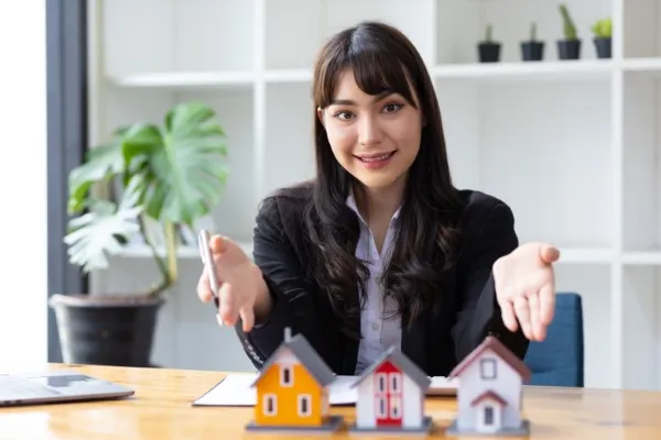 Emprendedora inversionista presenta opciones inmobiliarias con entusiasmo, mostrando pequeñas maquetas de casas sobre la mesa.