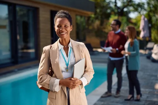 Una mujer sonriendo en donde se puede observar en el fondo unos clientes que ayudará con el asesoramiento.
